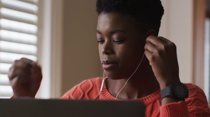 非裔美国妇女，在家工作时戴着耳机使用笔记本电脑