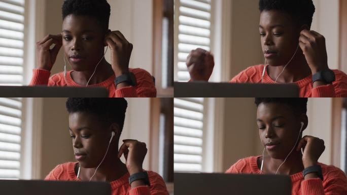 非裔美国妇女，在家工作时戴着耳机使用笔记本电脑