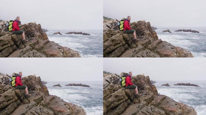 资深徒步者背着背包坐在岩石上，在海边徒步旅行。