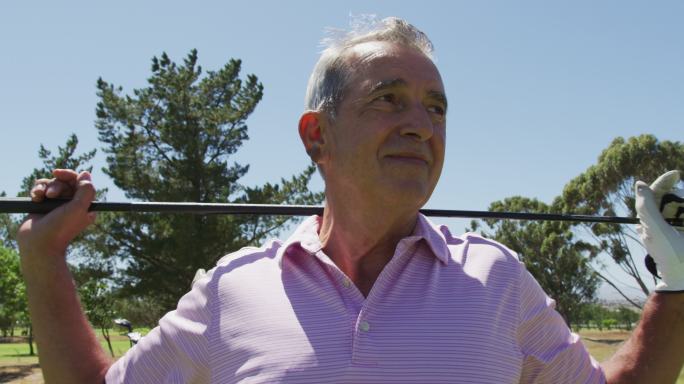 在一个阳光明媚的日子里，一个白人老人在高尔夫球场上用高尔夫球杆微笑