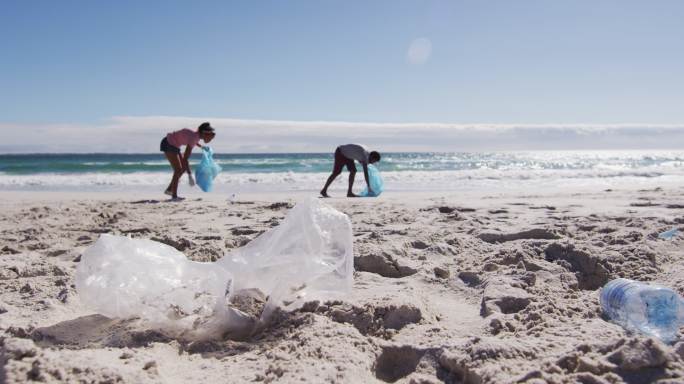 一对非洲裔美国夫妇拿着垃圾袋，在海滩上收集塑料垃圾