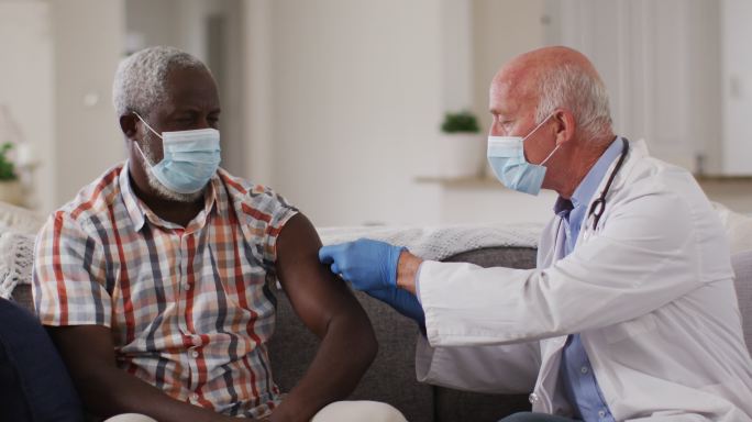 资深白人男性医生为资深非洲裔美国人接种疫苗在家都戴着口罩