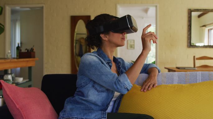 一个白人女人戴着虚拟现实头盔，坐在家里的沙发上