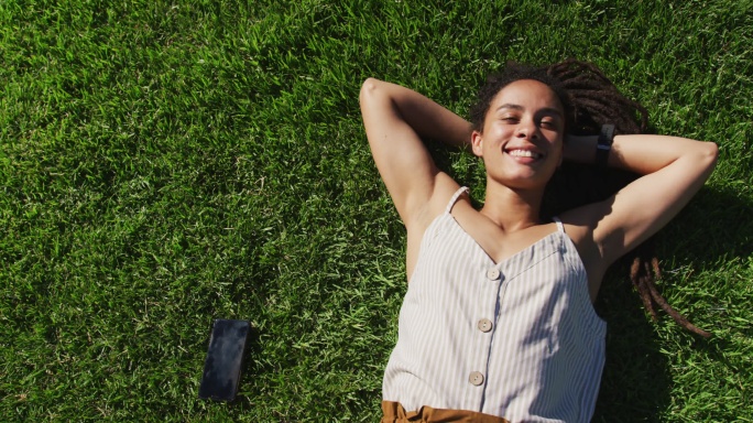 非裔美国妇女的肖像躺在草地上看着照相机微笑