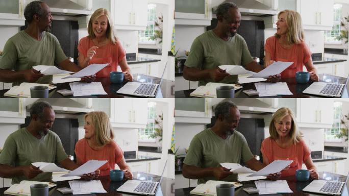 幸福的老夫妇使用笔记本电脑和支付账单在厨房