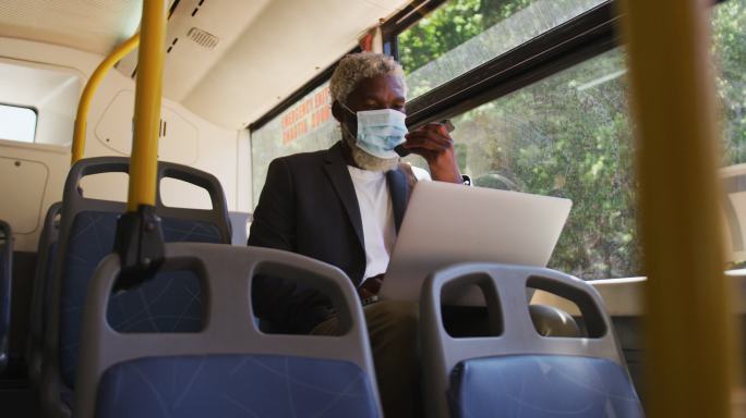 非洲裔美国老人戴着口罩，一边坐着一边用智能手机和笔记本电脑聊天