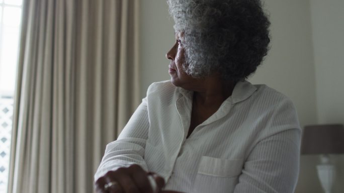 一位年长的非裔美国妇女拄着拐杖坐在家里的床上