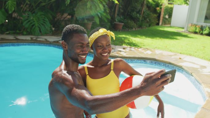快乐的非裔美国人夫妇站在游泳池自拍和微笑在阳光灿烂的花园