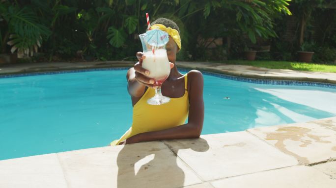 一个快乐的非洲裔美国妇女站在游泳池用她的饮料敬酒的肖像