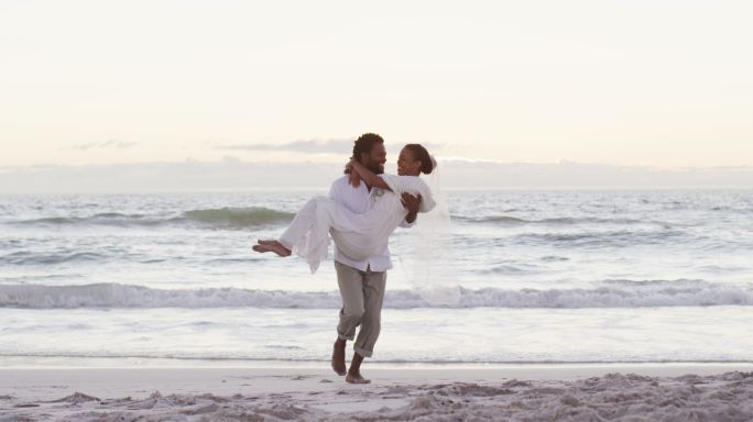 非裔美国情侣在结婚，男人抱着女人在日落的海滩上