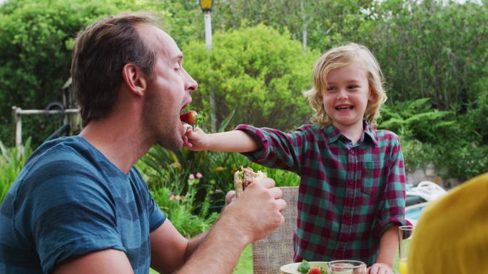 微笑的白人男孩喂他的父亲一个草莓在庭园家庭餐