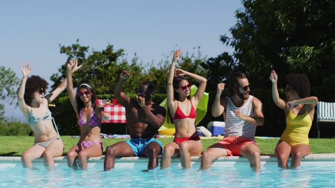 一群各式各样的朋友坐在泳池边跳舞和享受