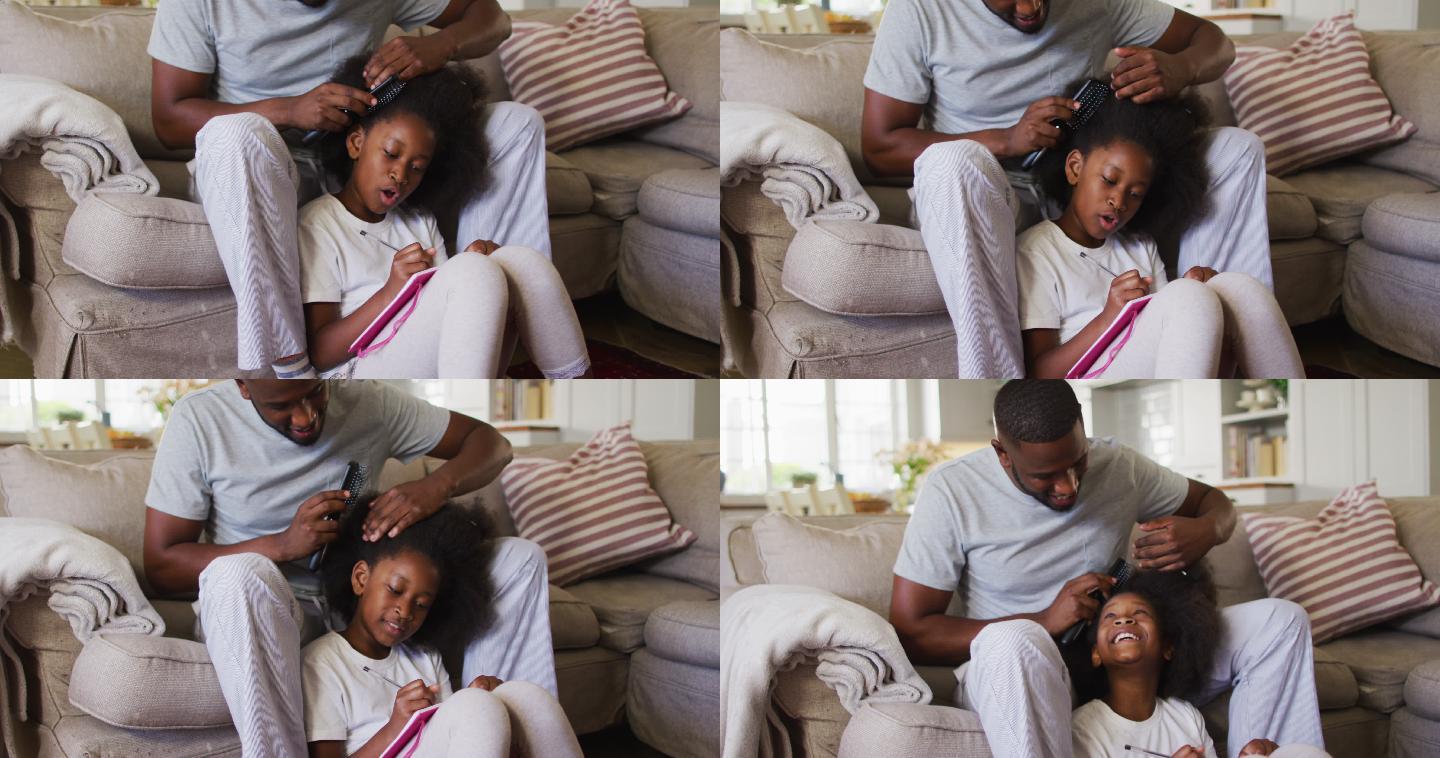 一位非裔美国父亲坐在家里的沙发上为女儿梳头
