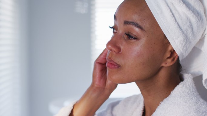 近距离的非洲裔美国妇女在浴衣清洁她的脸与棉垫在浴室