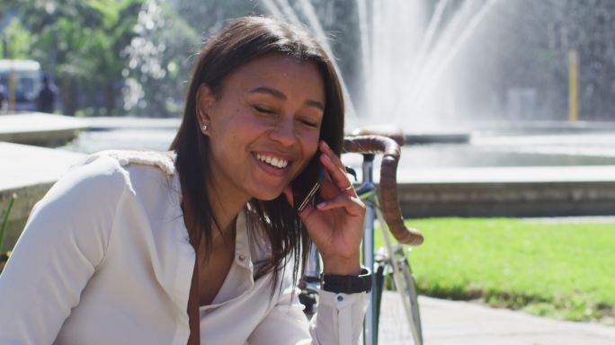 非裔美国妇女骑着自行车，坐在城市公园里用智能手机聊天