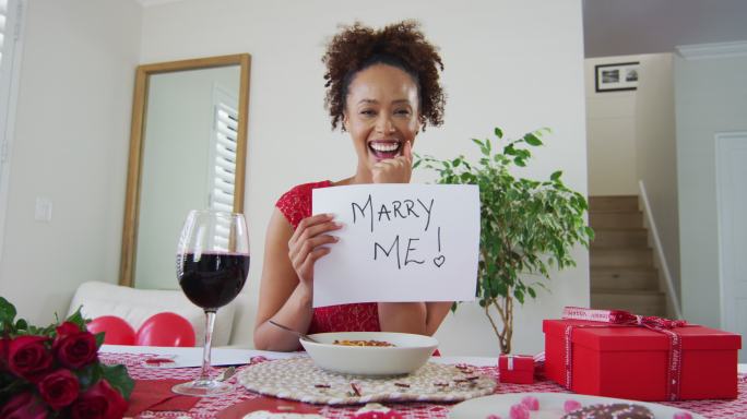 一名混血女子正在进行情人节约会视频通话，手里拿着“嫁给我”的求婚标志