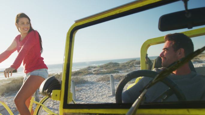 快乐的白人女人骑自行车旁边的男人在海边沙滩车