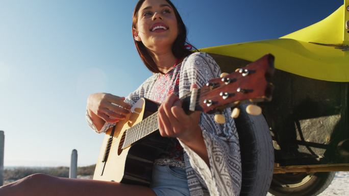快乐的白人女人坐在沙滩车在海边弹吉他