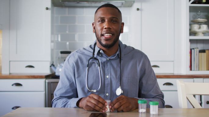 肖像的非洲裔美国医生拿着药物容器说话，同时有一个视频电话