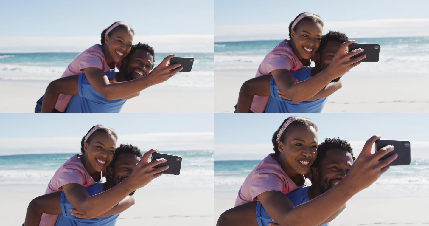 一对非裔美国夫妇用智能手机自拍，一名男子背着一名女子在海滩上