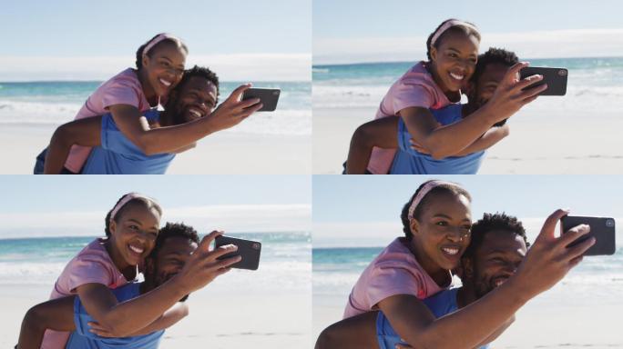 一对非裔美国夫妇用智能手机自拍，一名男子背着一名女子在海滩上