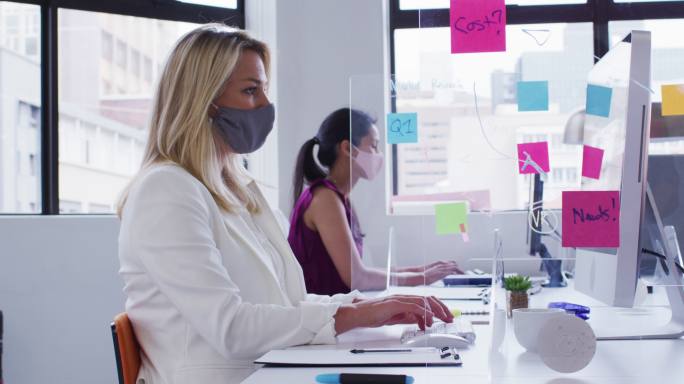 许多职场女性都戴着口罩在办公桌前工作，并在办公桌之间设置了卫生屏障