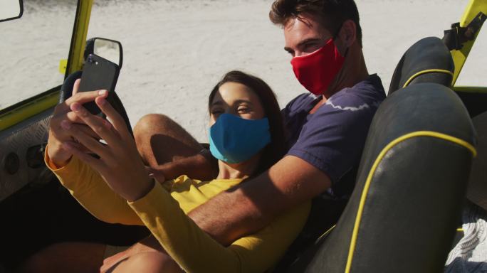 幸福的白人夫妇戴着面具坐在沙滩车自拍