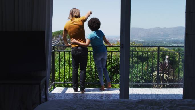 后视图，异族夫妇站在家中阳台欣赏风景