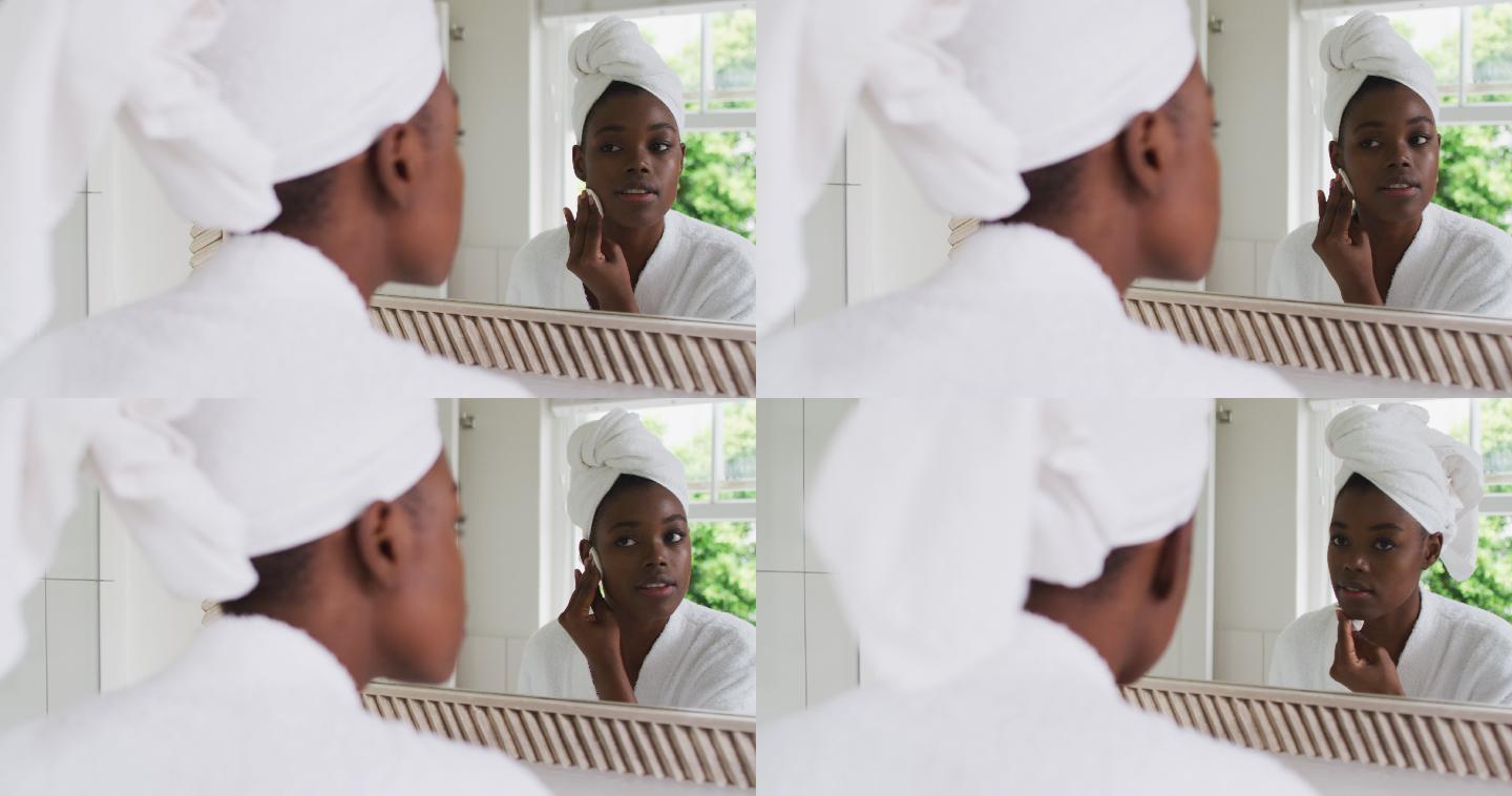非裔美国妇女在浴袍清洁她的皮肤与棉垫，而看着镜子