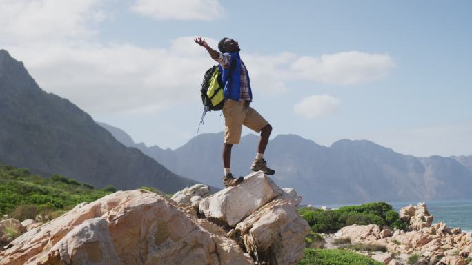 非洲裔美国人，站在岩石上，双臂张开，在山里徒步旅行
