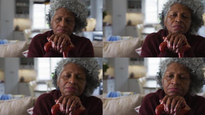 一位深思熟虑的非洲裔美国高级妇女拄着拐杖坐在家里的沙发上