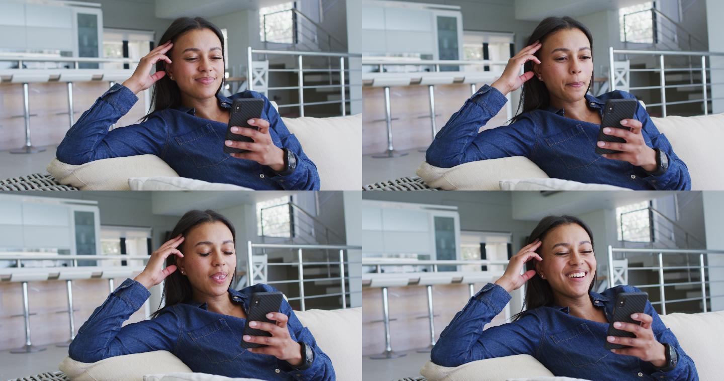 混血女子坐在沙发上用智能手机视频聊天大笑