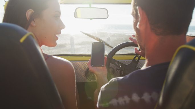 幸福的白人夫妇坐在沙滩车在海边使用智能手机