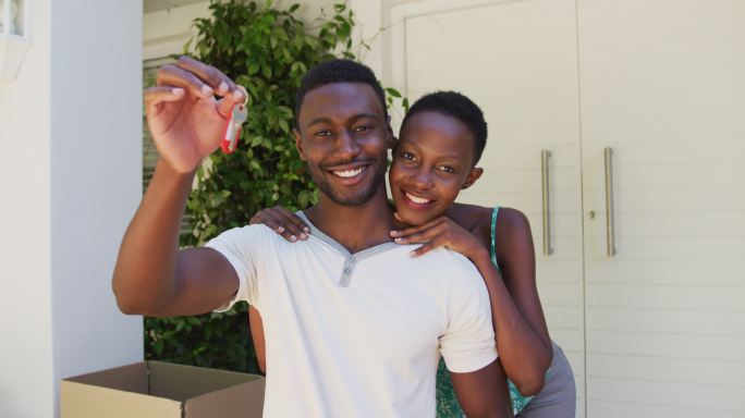 微笑的非裔美国夫妇拿着房子钥匙，在屋外拥抱