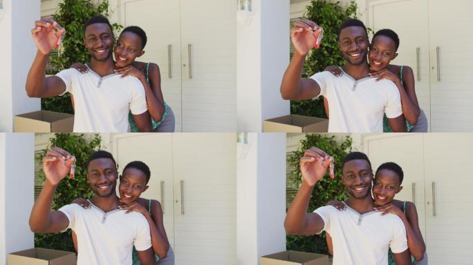 微笑的非裔美国夫妇拿着房子钥匙，在屋外拥抱
