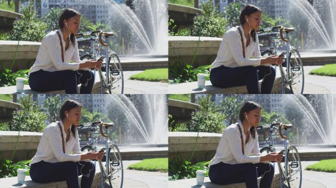 非裔美国妇女骑自行车戴着耳机在城市公园使用智能手机