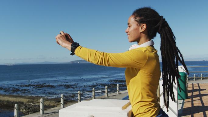 非裔美国妇女在海边散步时使用智能手机