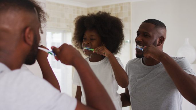 非洲裔美国人的女儿和她的父亲看着镜子在浴室里一起刷牙