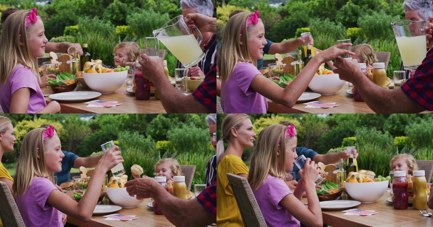 微笑的白人女孩喝柠檬水在家庭庆祝餐在花园里