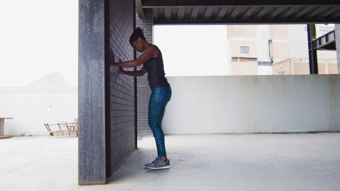 非裔美国妇女伸展倚在一堵墙在一个空的城市建筑