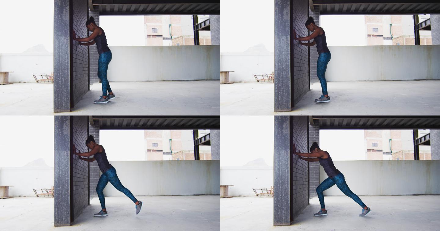 非裔美国妇女伸展倚在一堵墙在一个空的城市建筑