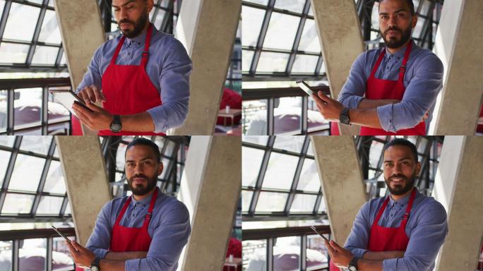 混血男性咖啡馆老板的肖像使用平板电脑和看着相机