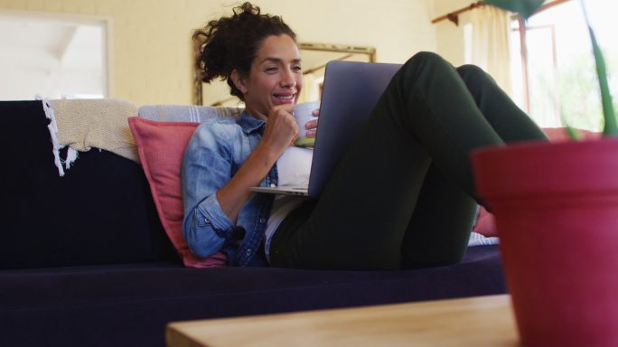 一个微笑的白人女人坐在家里的沙发上，用笔记本电脑进行视频通话