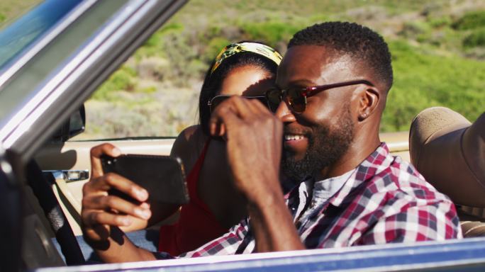 一对非洲裔美国夫妇在路上坐在敞篷车里使用智能手机
