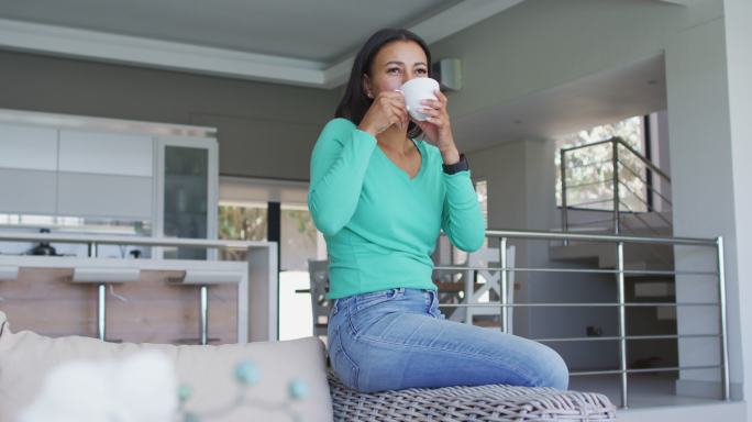 一位非裔美国妇女坐在家里的沙发上喝咖啡