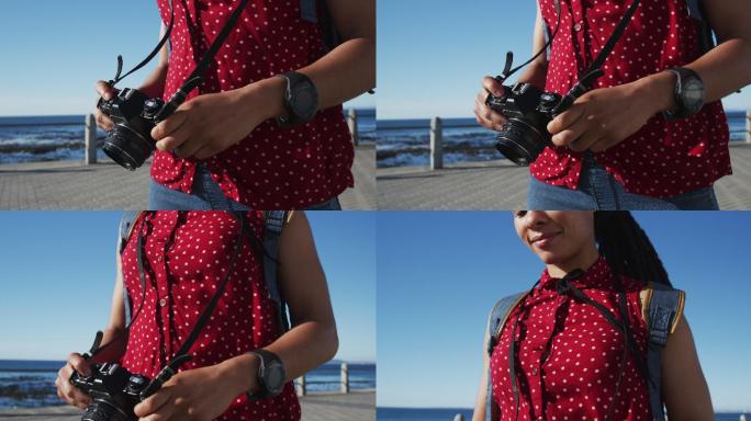 非裔美国妇女站在海边散步，拿着相机