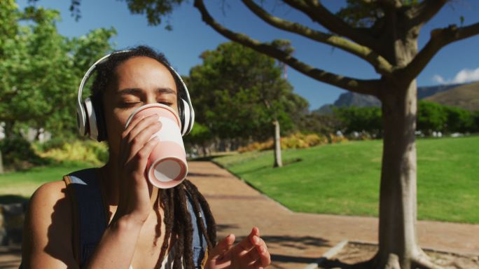 一位戴着耳机坐在公园里喝咖啡的非裔美国妇女