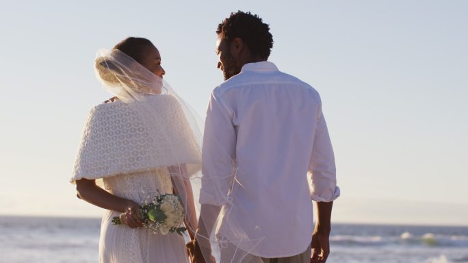 相爱的非裔美国人结婚了，互相看着对方，在海滩上牵着手