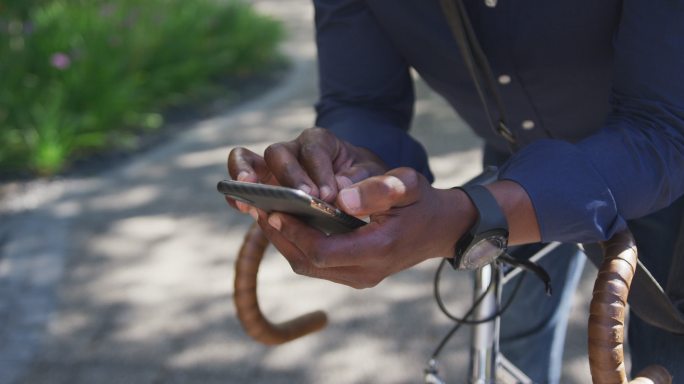 非裔美国老人戴着口罩，倚靠在自行车上使用智能手机