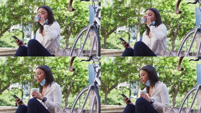非裔美国妇女戴着口罩用智能手机在城市公园喝咖啡